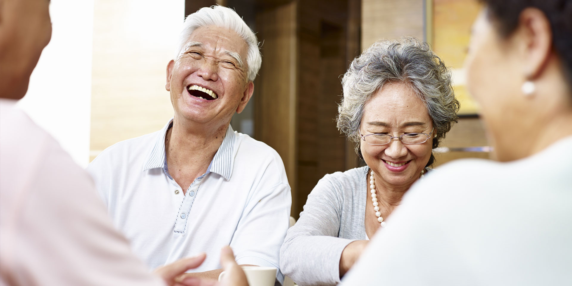 Elderly Asian friends laughing and talking at a table.